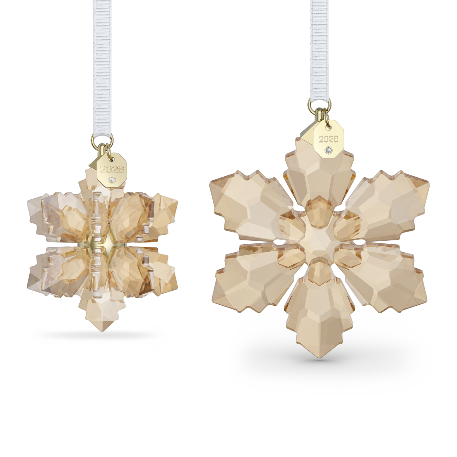 Two faceted snowflake ornaments in a pale champagne-gold tone, shown hanging against a white background. One ornament is turned to show the side with a white hanging ribbon and a small gold tag engraved with '2028'; the other is shown from the front.