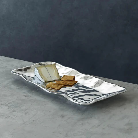 Silver wavy plate with crackers and cheese on a gray surface and dark background