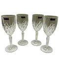 Four clear cut-crystal wine glasses with faceted stems and circular bases, arranged on a white cloth against a beige wall.