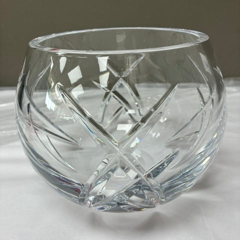 A clear cut-crystal tumbler with a faceted geometric pattern, resting on a white surface against a neutral gray background.