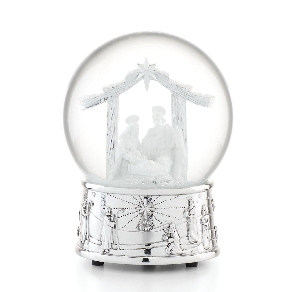 A clear glass Christmas snow globe with a silver-toned base, featuring a white nativity scene inside with a stable, star, and small figurines, photographed on a white background.