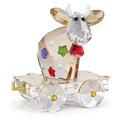 A faceted crystal cow figurine with white horns, seated on a clear crystal cart with gold-toned hardware, decorated with colorful star and dot accents, photographed on a white background.