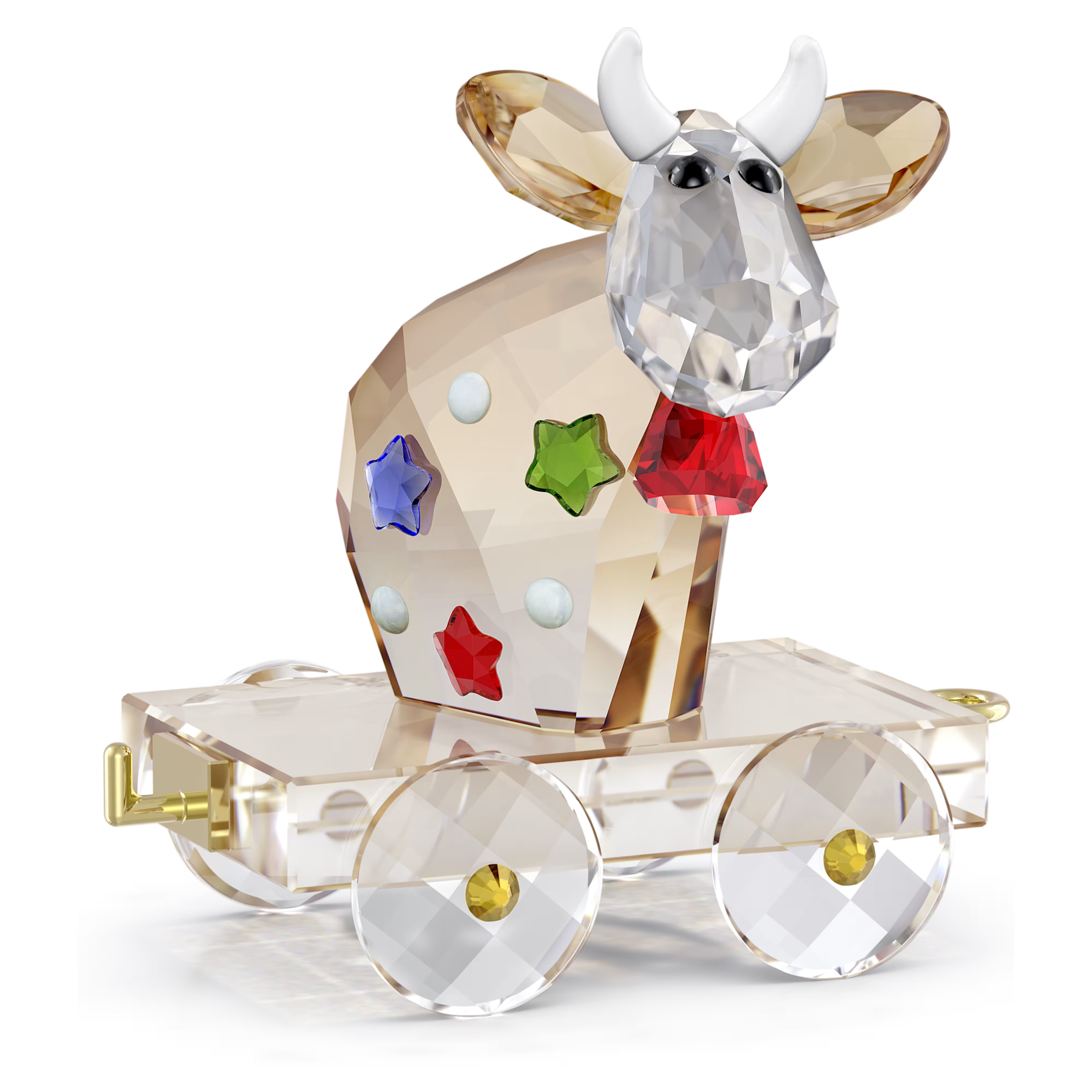 A faceted crystal cow figurine with white horns, seated on a clear crystal cart with gold-toned hardware, decorated with colorful star and dot accents, photographed on a white background.